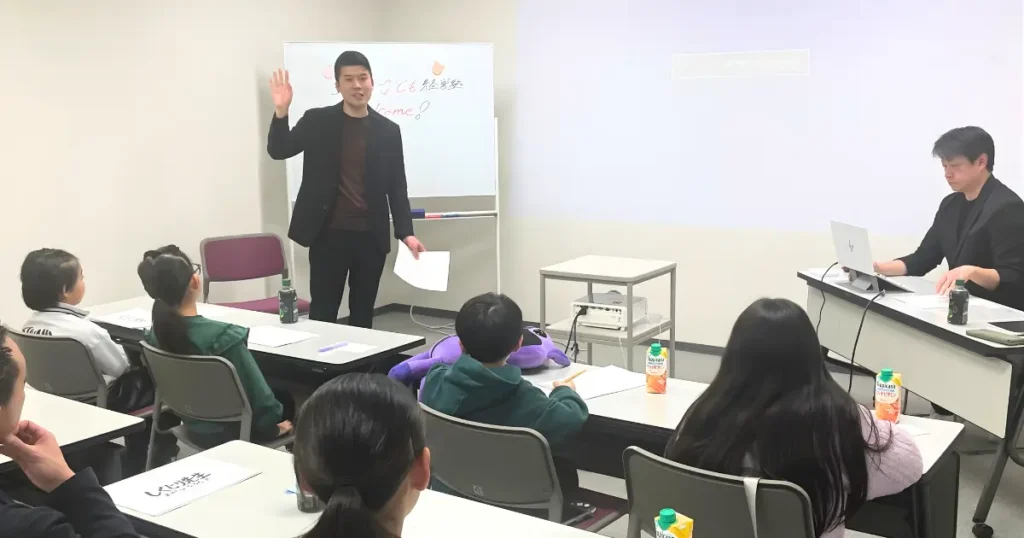 桜花ライフアカデミーの講義風景。代表の石井が子どもたちの前で語りかけ、メンターの鶴谷がサポートしている様子