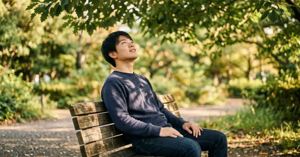 朝の公園のベンチで空を見上げる若い男性