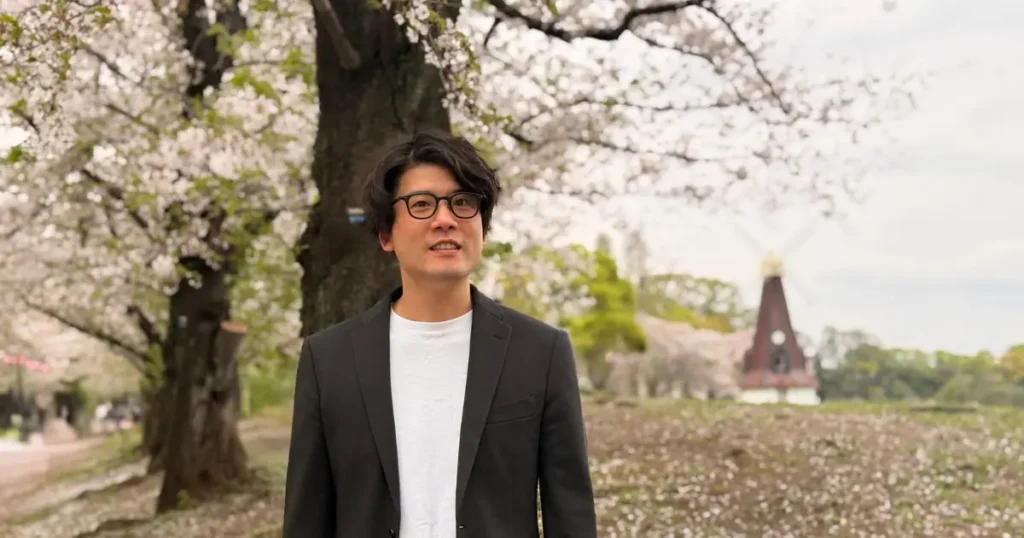 桜花ライフアカデミー代表の石井豊が桜が咲く木の下に立っている